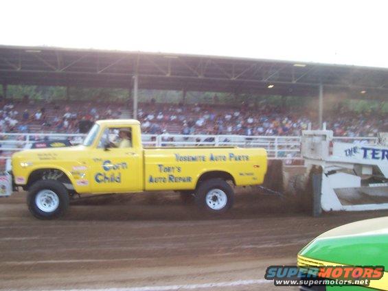 Yellow pickup truck named 'The Corn Child' pulling a sled at a competition
