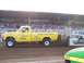 1994 Ford F-150 - A yellow pickup truck competes in a pull event, with spectators in the background.