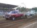 1994 Ford F-150 - A red pickup truck competes in a pull event, dragging a trailer across a dirt track.