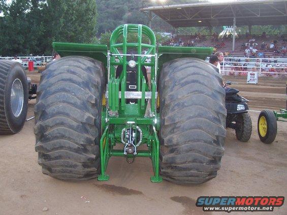 Rear view of a green tractor puller with massive tires and a roll cage
