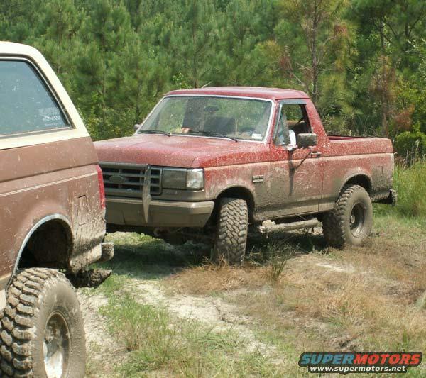 Red pickup truck and brown SUV parked on dirt road with trees in background