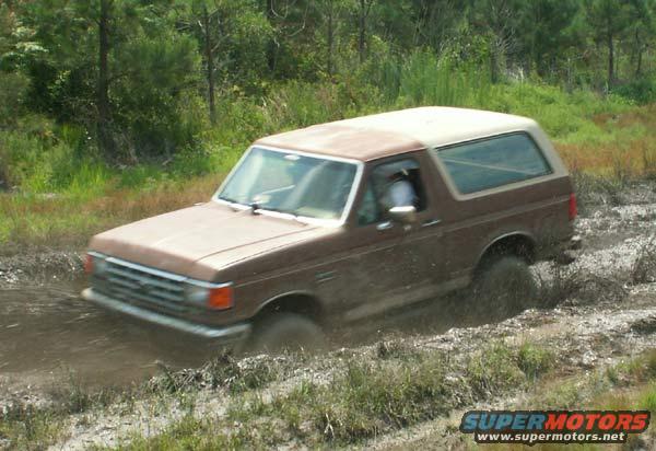 Brown 1988 Ford Bronco driving through mud