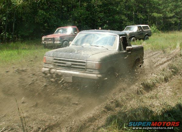 Muddy 1987 Ford Bronco and two pickup trucks driving off-road