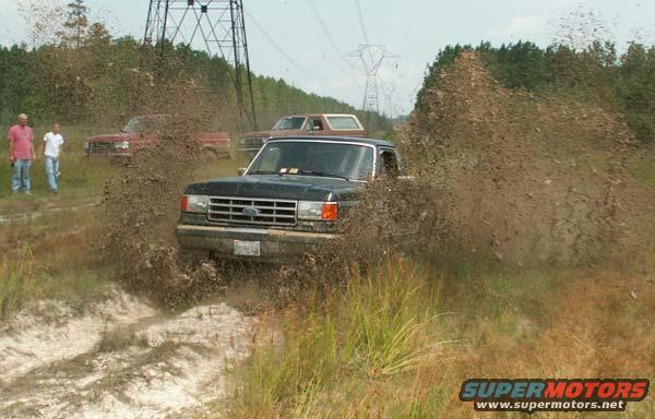 Black Ford F-Series truck splashing mud, front view. License plate visible