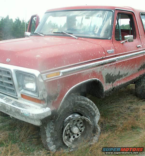 Red Ford Bronco with a damaged front wheel stuck in mud