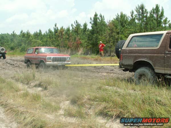 Red 1978 Ford Bronco stuck in mud, being towed by brown Bronco
