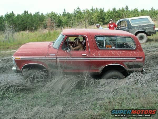 Red 1978 Ford Bronco stuck in mud, side view. Mud splatters on body