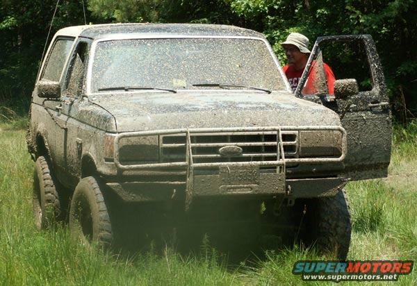 Muddy SUV with door open, person in hat and red shirt standing by it