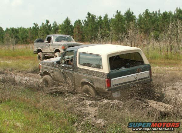 Two Ford Broncos stuck in mud, one in foreground with white top, other behind it