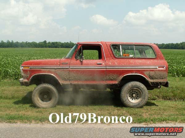 Red Ford Bronco with mud splatters, side view, in a field