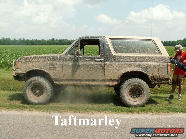 muddy SUV parked on grass, person with bag stands nearby