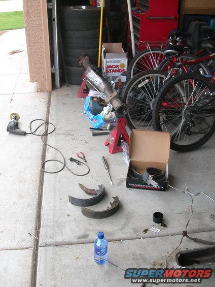 Tools and parts laid out on garage floor, including brake shoes, a grinder, and a catalytic converter on jack stands