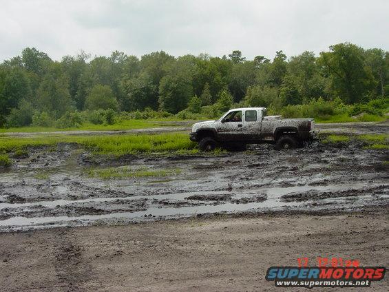 White pickup truck stuck in mud pit with trees in background