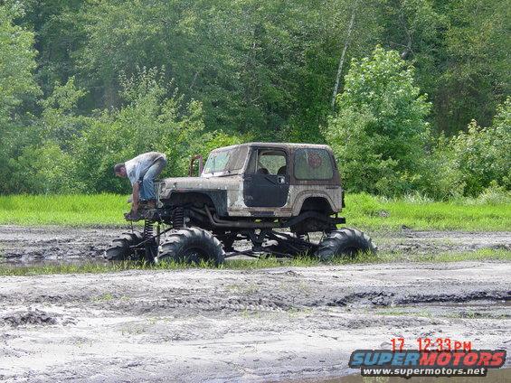Modified Jeep Wrangler with large tires in mud, person working on front