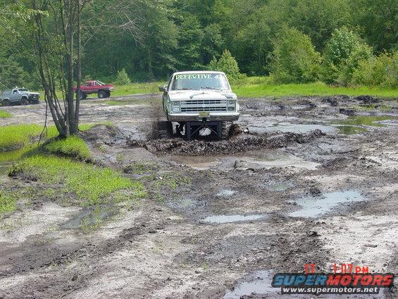 White pickup truck with "DEFECTIVE 4" on windshield stuck in mud