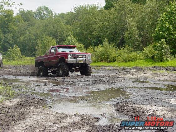 Red lifted pickup truck driving through mud with large tires