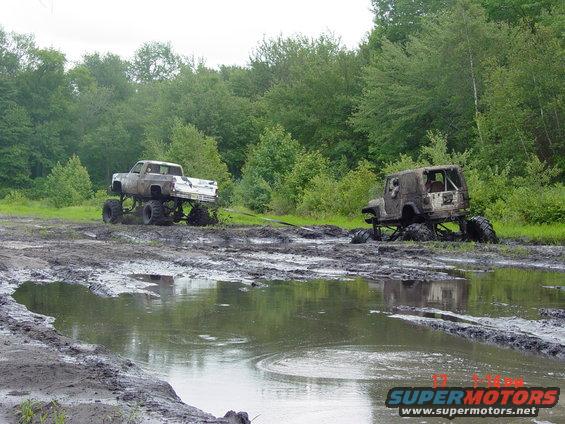 Muddy truck and Jeep stuck in a swampy area with trees in the background