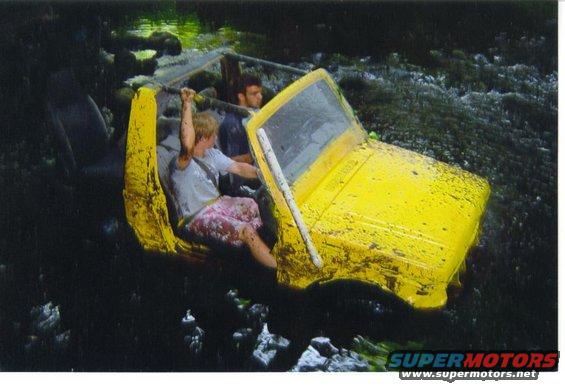 Yellow off-road vehicle with two people submerged in dark water, mud splattered