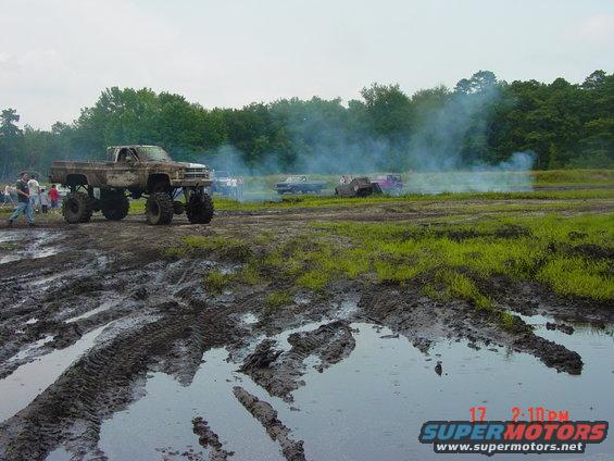 Lifted pickup truck with large tires in a muddy field, smoke in background