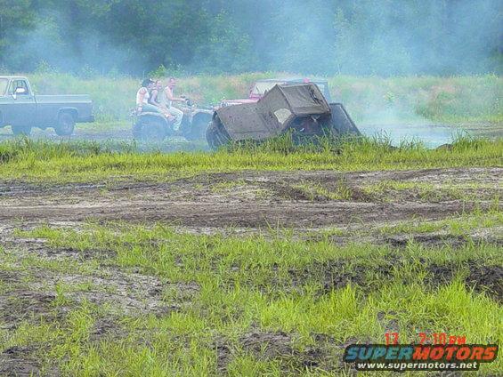 ATV with three people stuck in mud, with a pickup truck nearby