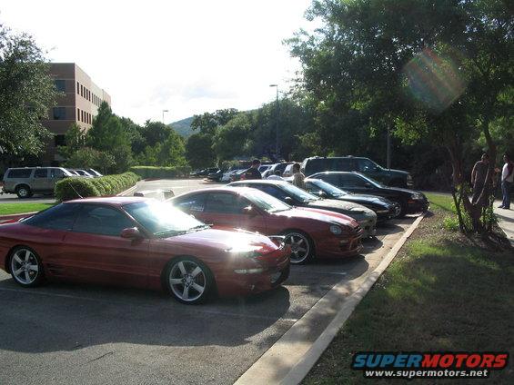 Red coupe parked in a lot with other cars and a building in the background