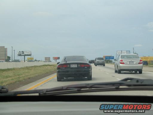Black sedan from rear, driving on highway. License plate visible