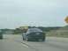 1994 Ford Probe - A black 1994 Ford Probe is seen from behind while driving on a highway under an overcast sky.