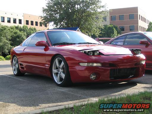 Red 1994 Ford Probe coupe parked in a lot, front 3/4 view. The car has pop-up headlights and aftermarket wheels