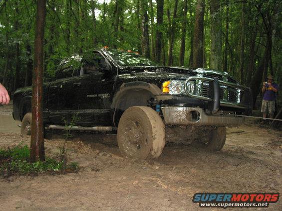 Black Dodge Ram pickup truck stuck in mud, front wheel deep in mud, trees in background