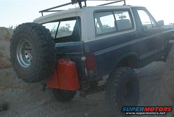 Dark blue and white Ford Bronco with a spare tire and two red jerrycans mounted on the rear