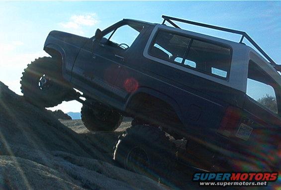 Dark blue SUV with off-road tires climbing a rocky incline, sun glare on windshield
