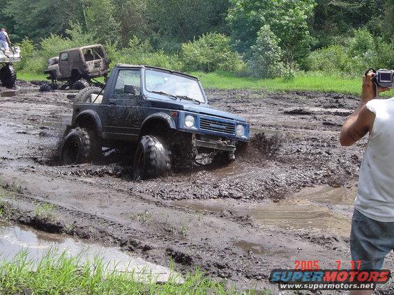 Blue off-road vehicle with large tires stuck in mud, another vehicle in background