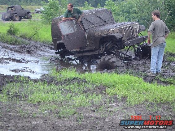Mud-covered Jeep Wrangler stuck in mud with two men standing nearby
