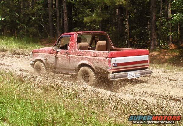 red SUV driving through mud, tires kicking up dirt