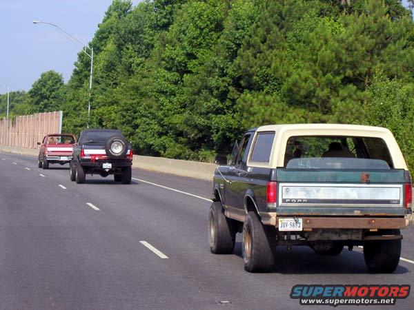 Dark green and tan Ford Bronco with a spare tire on the back, driving on a highway