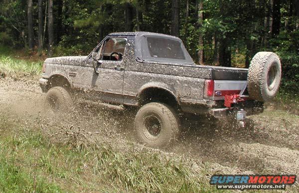 Mud-splattered 1988 Ford Bronco driving through mud, rear tire visible