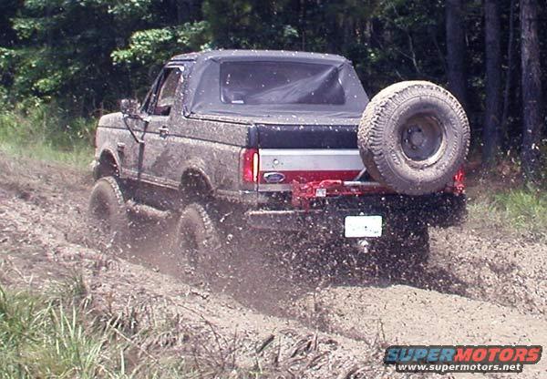 1988 Ford Bronco with soft top, driving through mud with spare tire mounted on rear