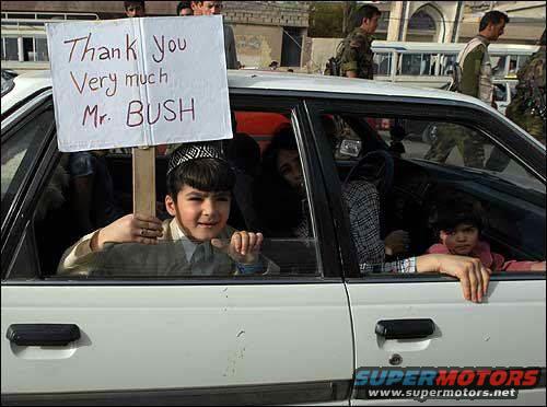 White sedan side view with children inside holding a sign that says "Thank You Very Much Mr. BUSH"