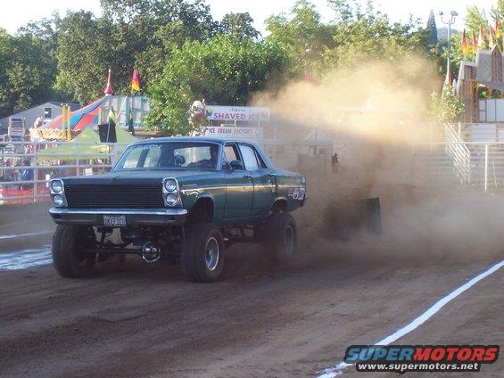 Green monster truck kicking up dust during a pull. License plate reads GKE316