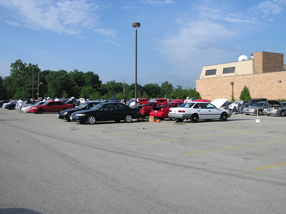Cars parked in a lot with a building and trees in the background