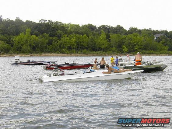 White boat with people relaxing on a lake, other boats in background