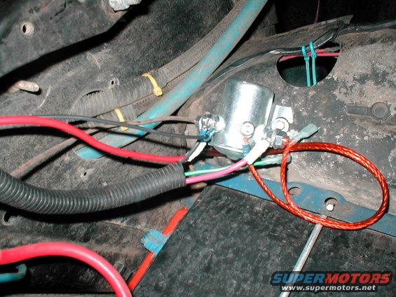 Close-up of a silver electrical relay with red, black, and blue wires connected, attached to a dark metal surface