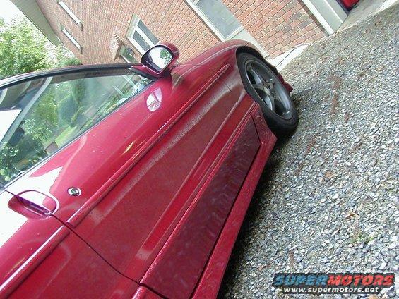 Red car side door and fender detail, parked on gravel