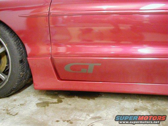 Red car side panel with a grey GT badge and a portion of the front tire visible