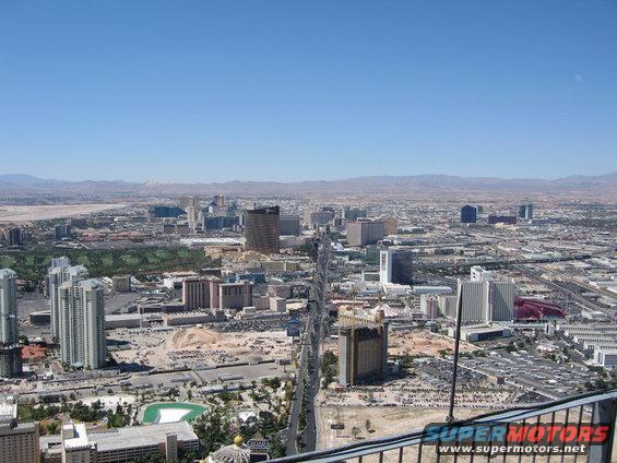 View of Las Vegas Strip with hotels and mountains in background. Watermark says SUPER MOTORS