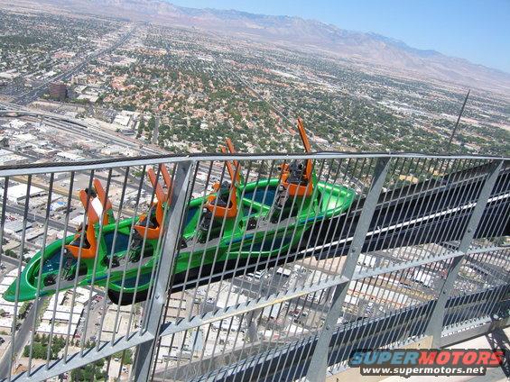 Green roller coaster car with orange seats on a track high above a city