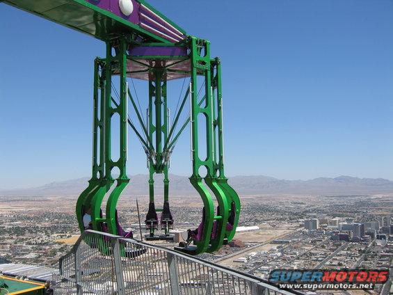 Amusement ride structure with seats suspended over a city skyline and mountains in the distance
