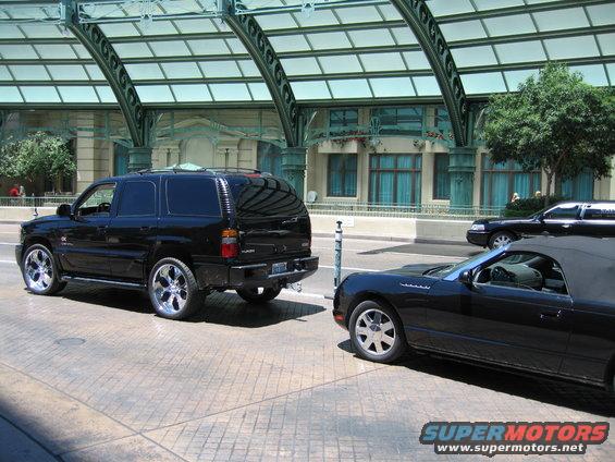 Black SUV parked next to a black convertible with a building and trees in the background