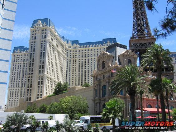 White limousine, bus, and SUV parked in front of a large hotel with a Paris Eiffel Tower replica