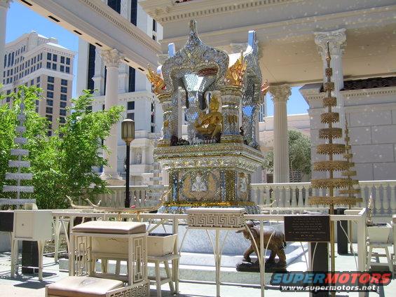 ornate shrine with golden Buddha statue, elephant statue, and tiered decorations in front of tall buildings